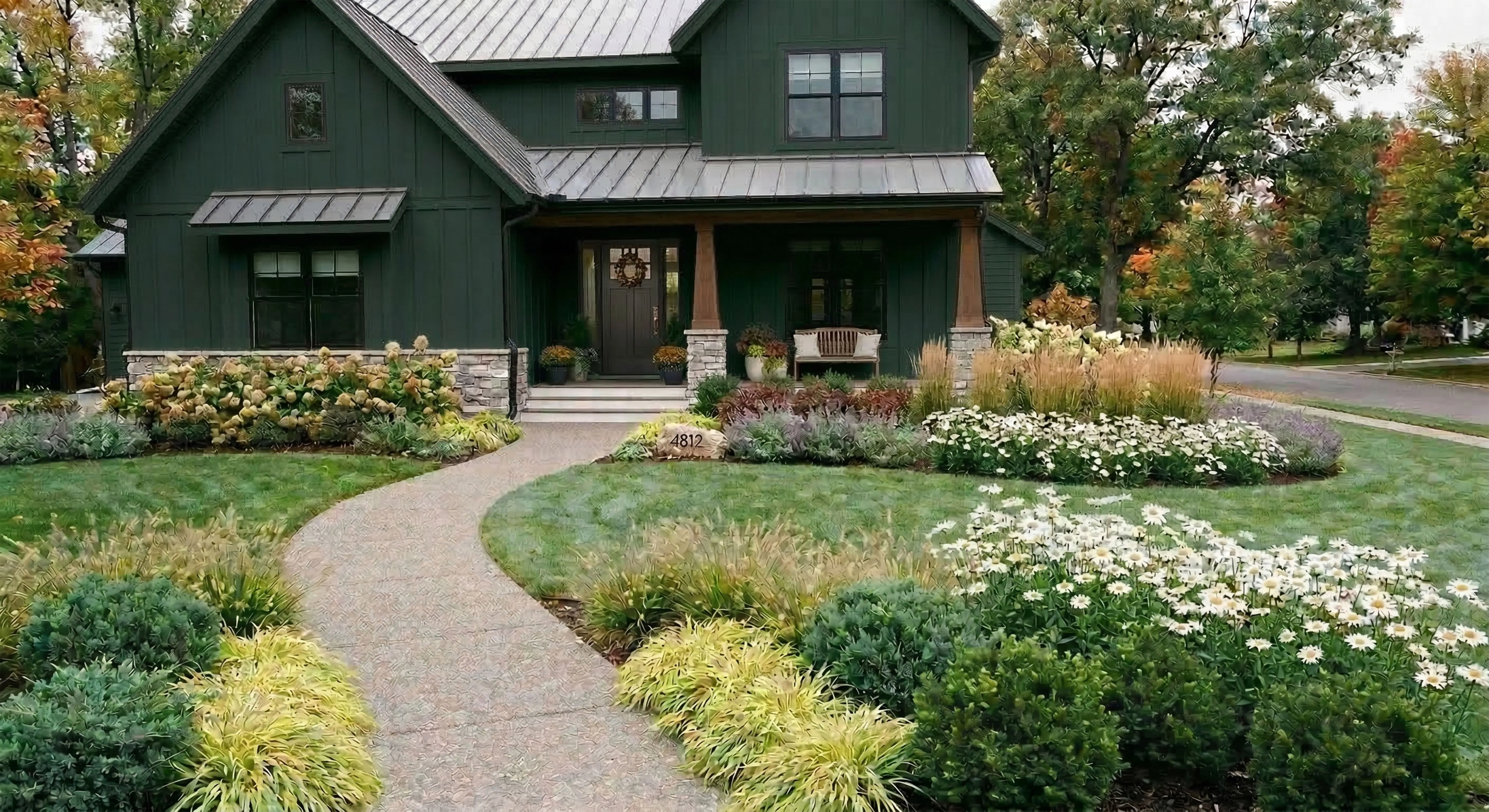 Dark forest green barn-style house with golden Japanese forest grass, white Shasta daisy drifts, and bronze ornamental grasses in fall
